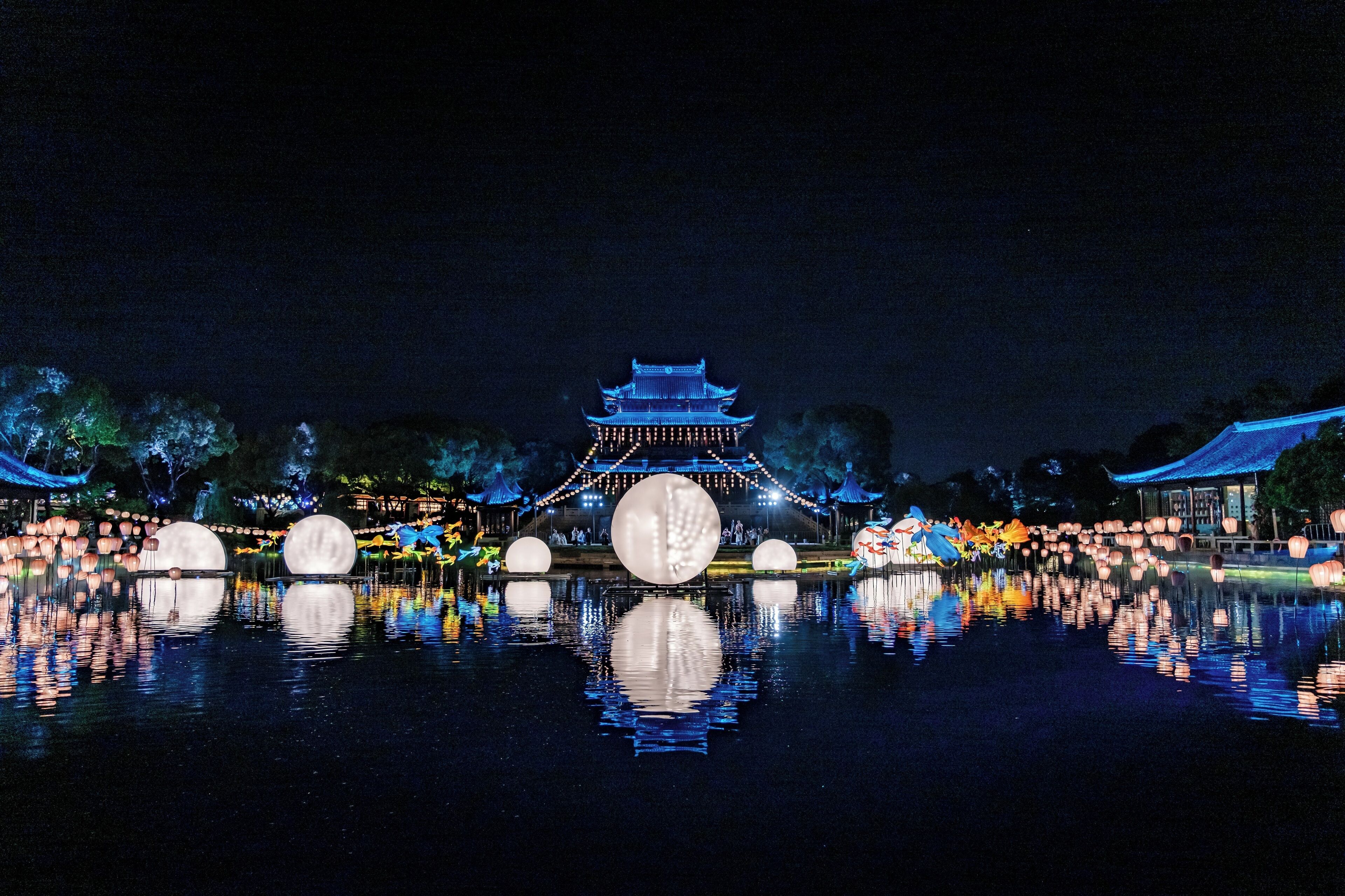 A traditional building with a central tower, surrounded by a reflective water body with floating spherical objects.
