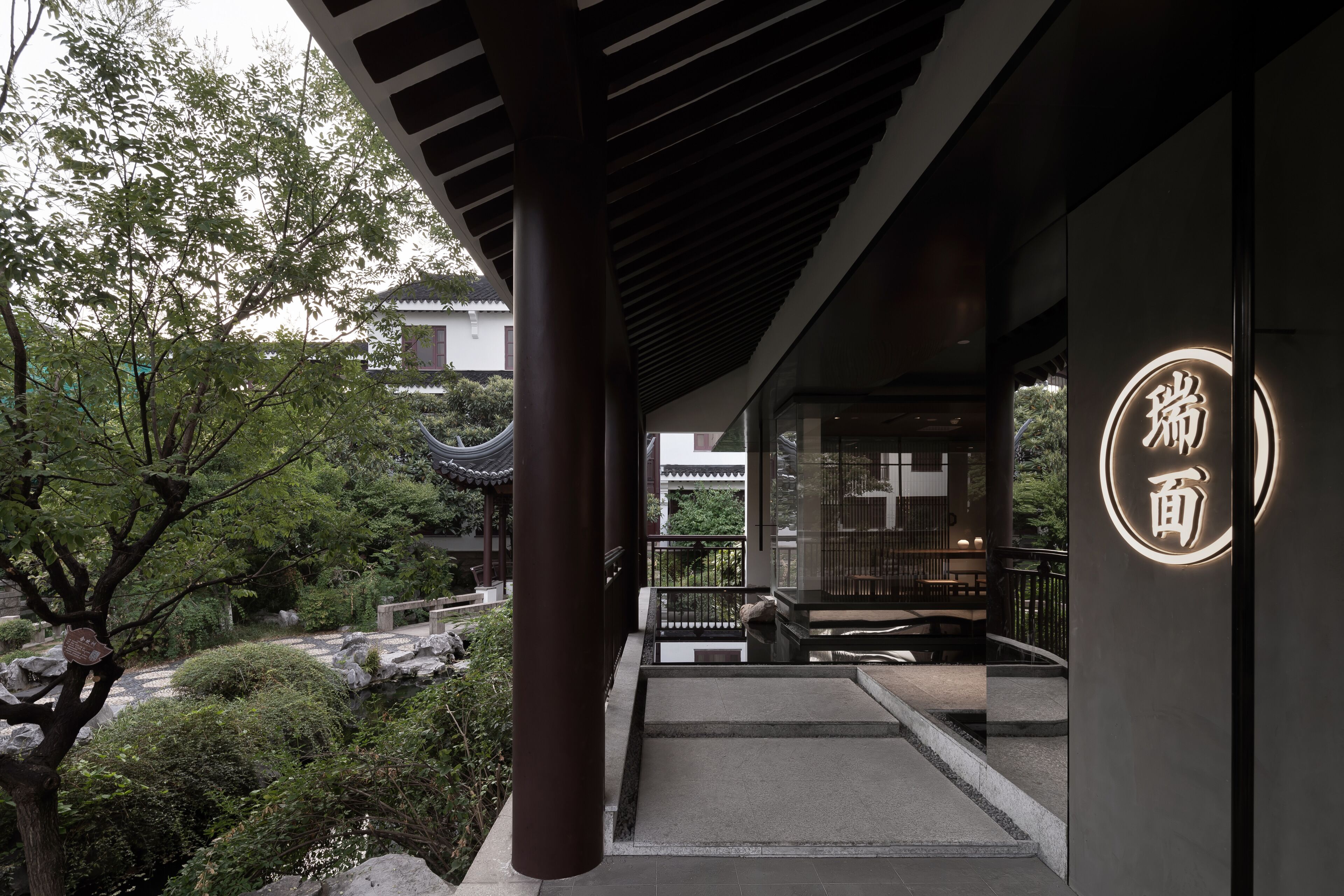 A modern building with a traditional Asian architectural style, featuring a stone pathway, wooden pillars, and a well-maintained garden with rocks and trees.