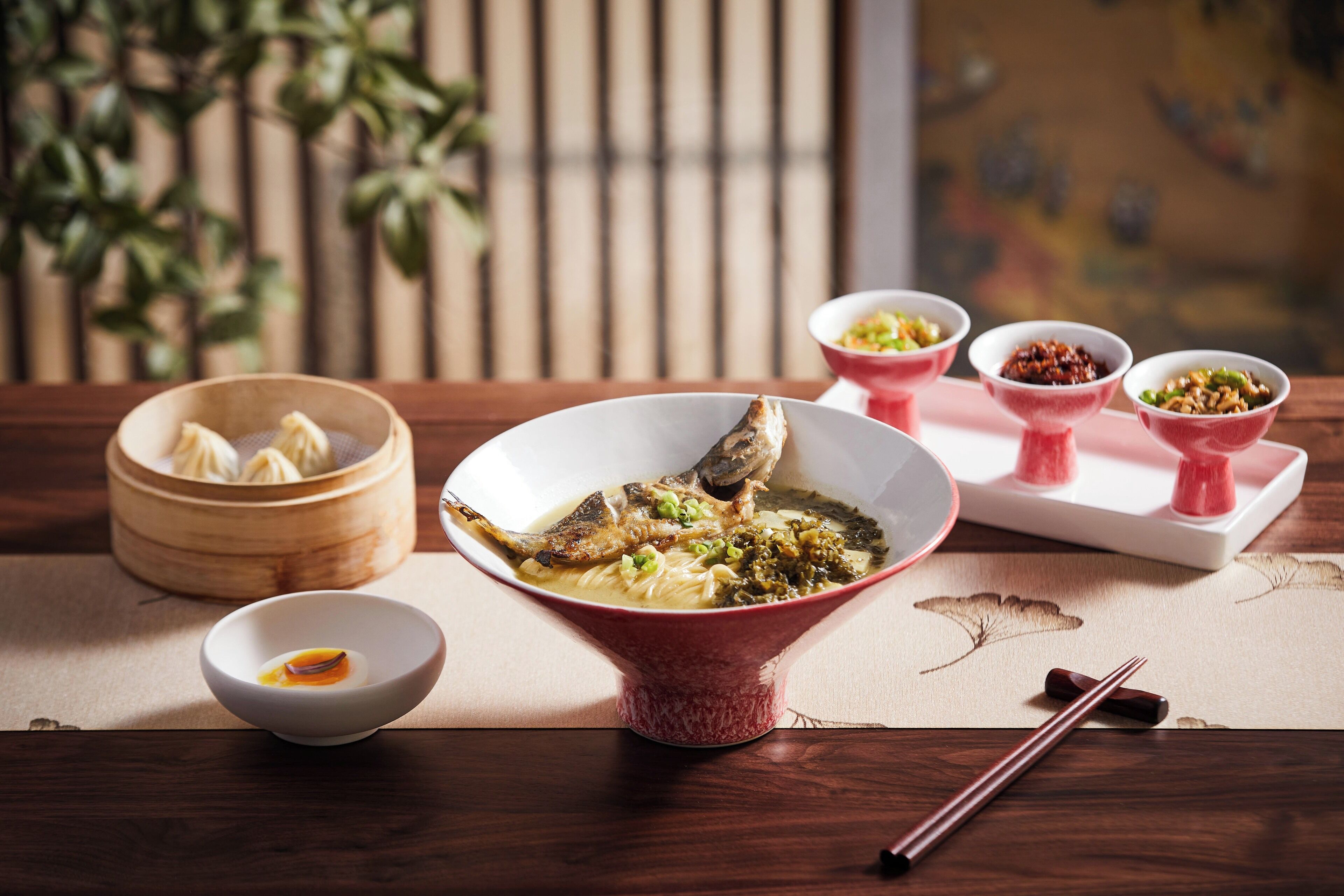 A dining table with a bowl of soup, a bowl of dumplings, and several small dishes of condiments.