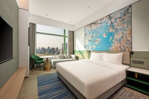 A modern hotel room with a large bed, a desk, a chair, and a view of the city skyline.