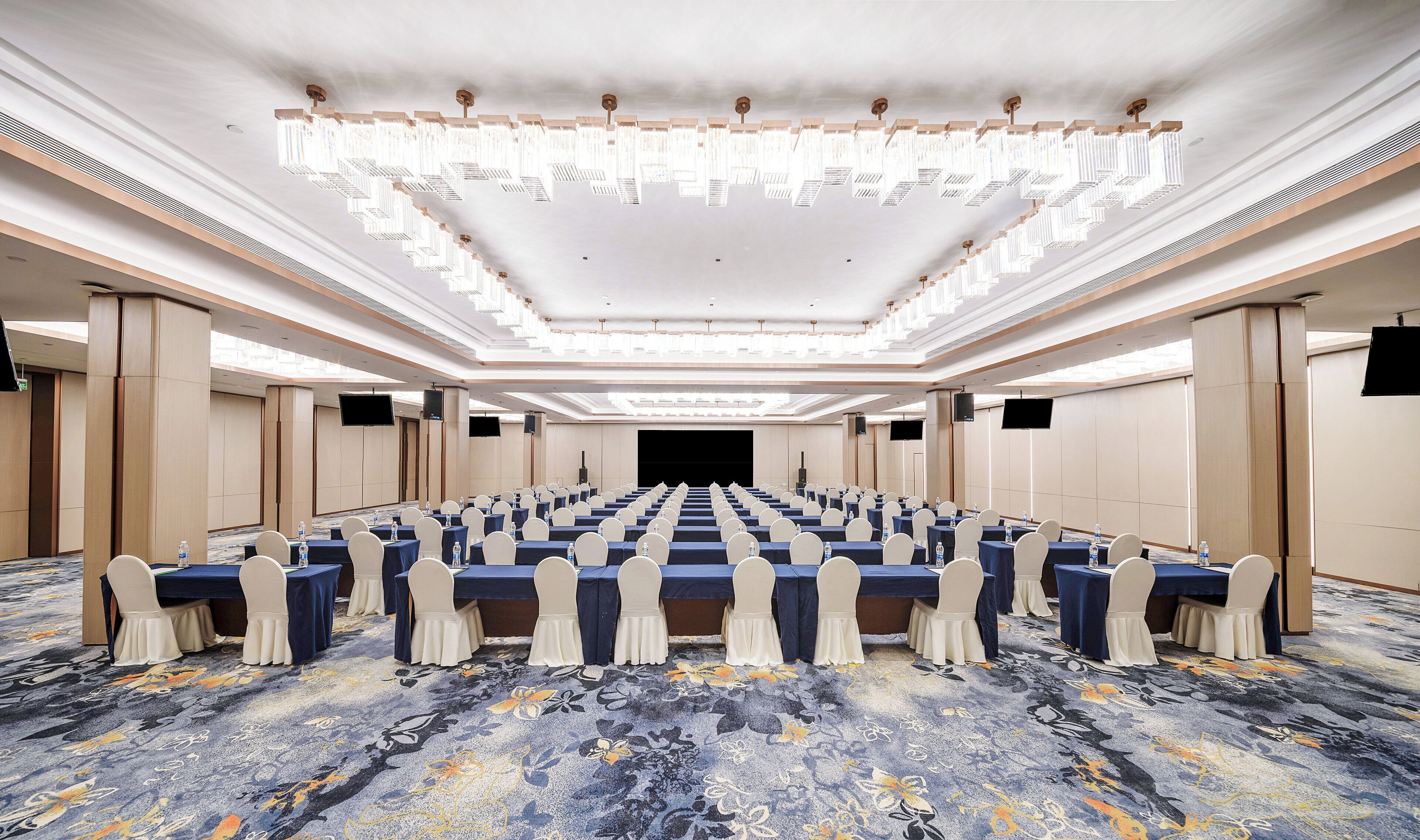 A conference room with rows of tables, chairs, and a large screen at the front.