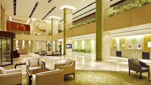 A spacious lobby with a reception desk, seating area, and a glass staircase connecting two floors.