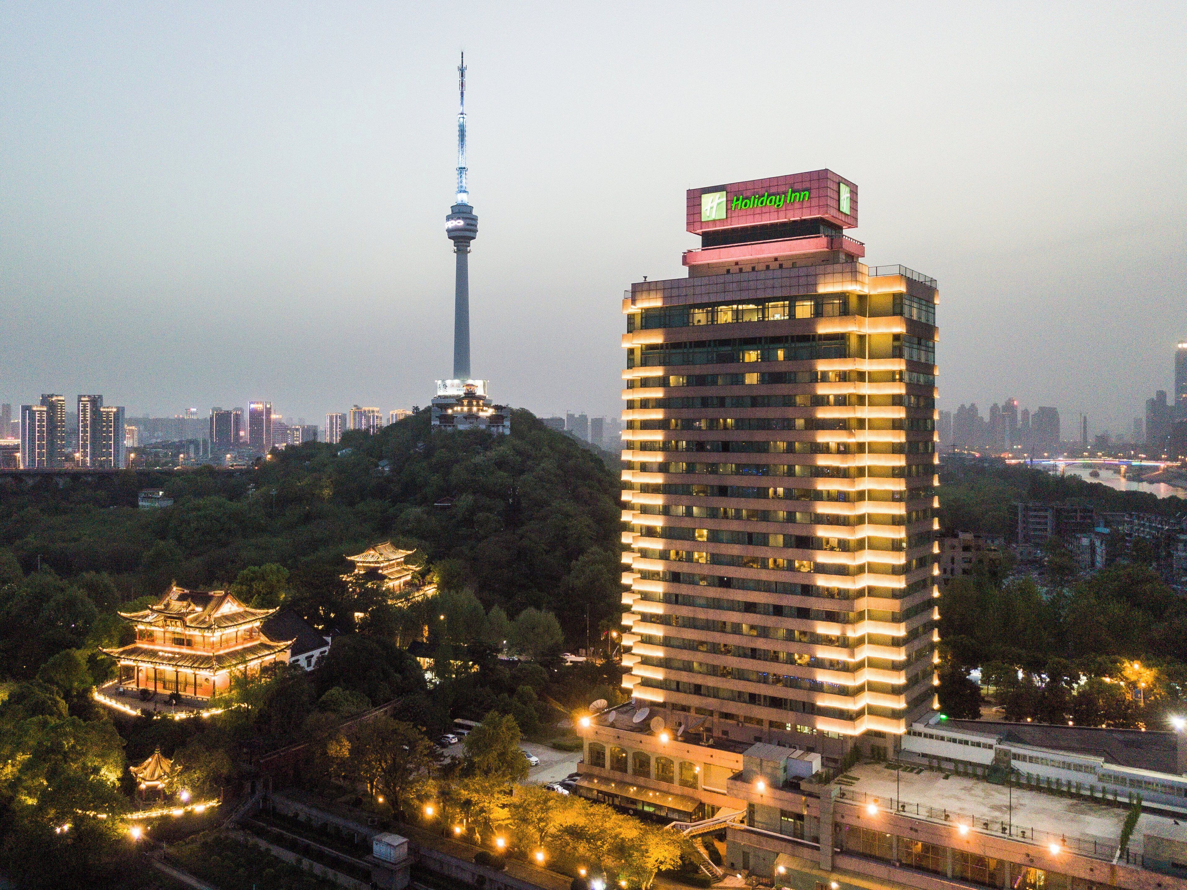Un edificio de gran altura con el letrero de Holiday Inn, rodeado de follaje y arquitectura tradicional.
