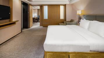 A hotel room with a large bed, a TV on a shelf, a desk, and a chair.