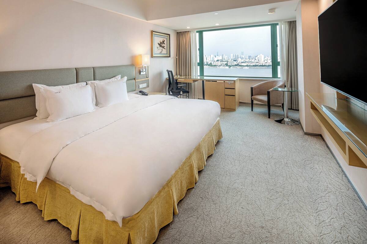 A hotel room with a large bed, a desk, a chair, and a TV.