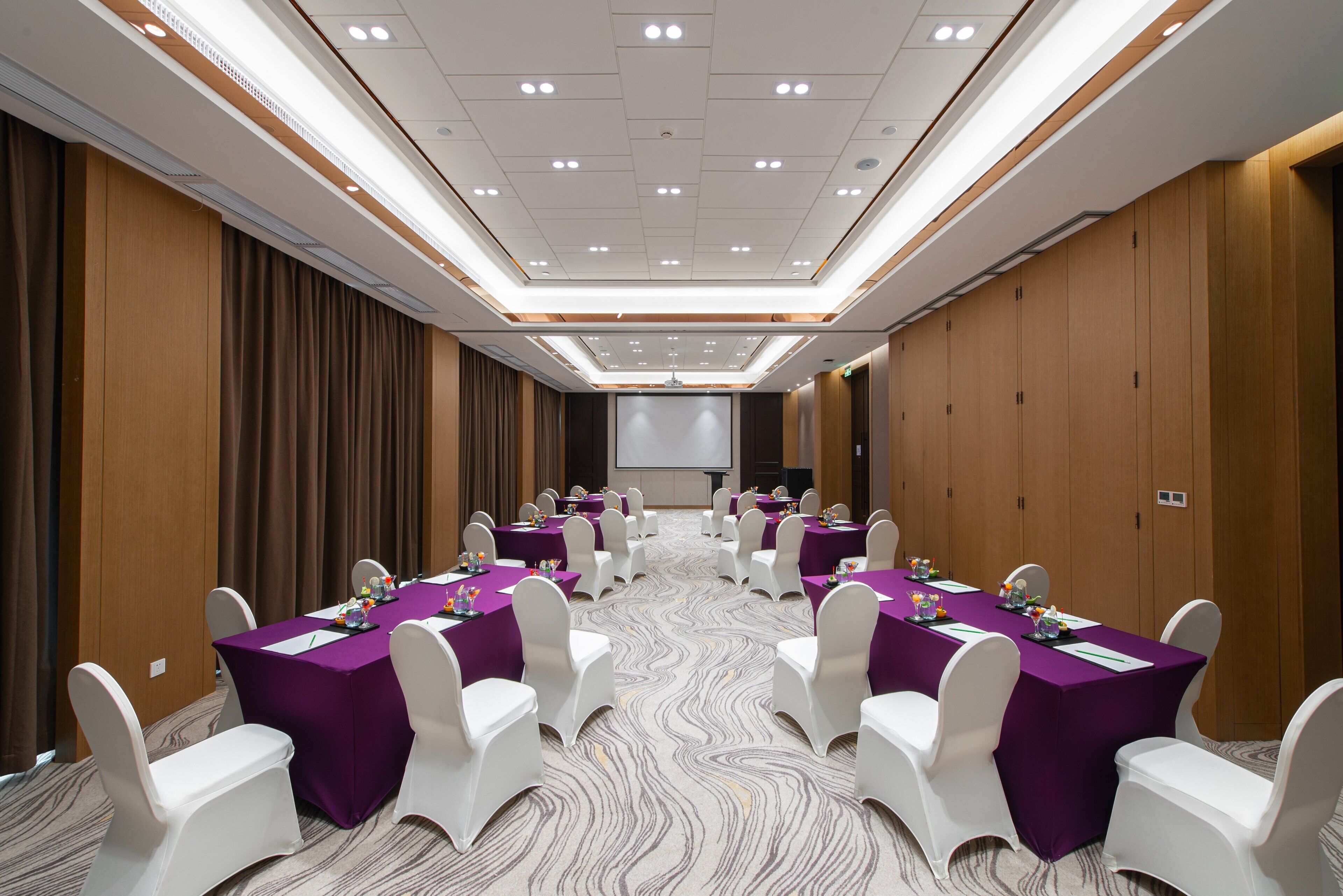 A conference room with a long table, white chairs, and purple tablecloths.