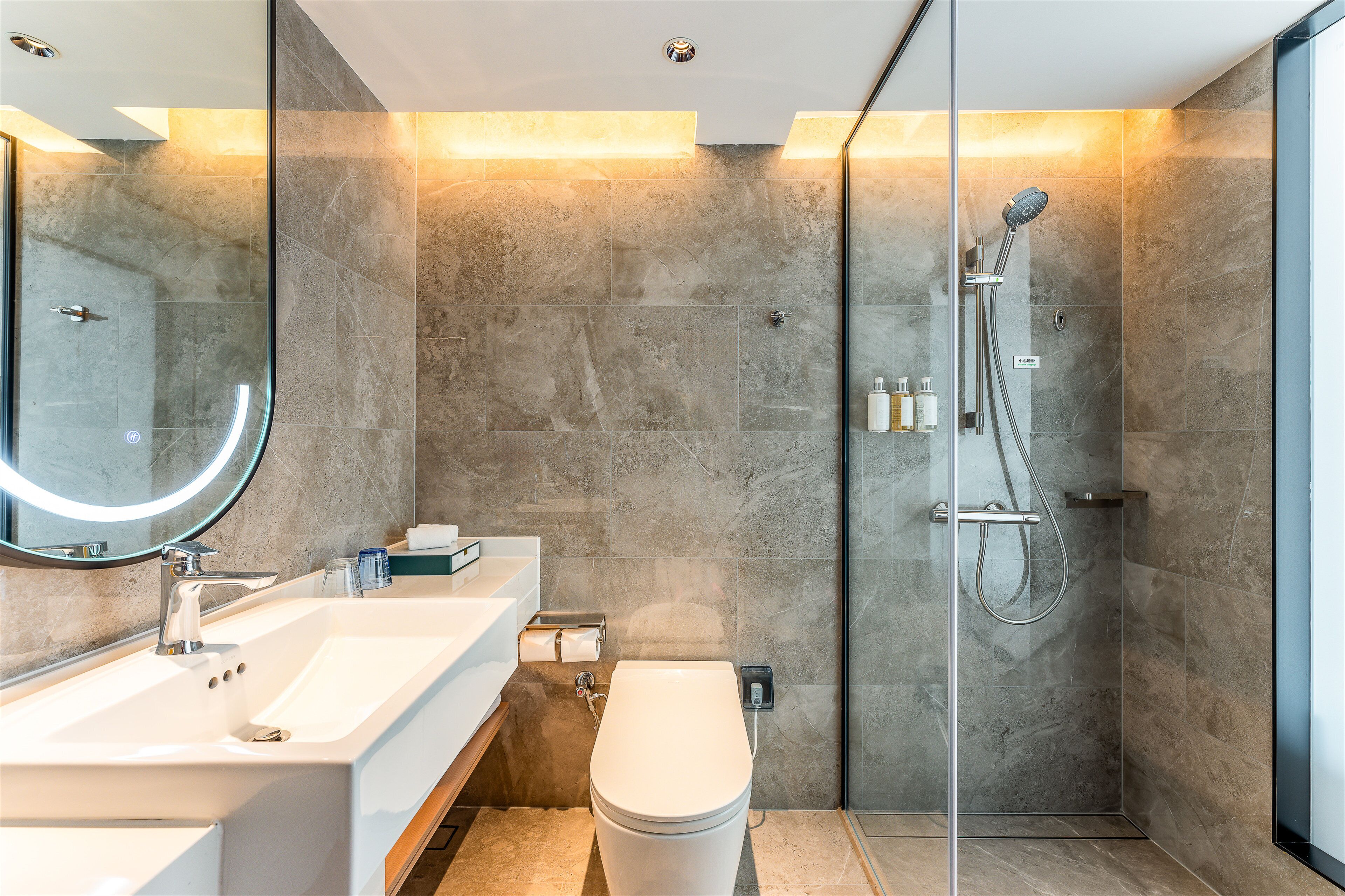 Un baño moderno con ducha envuelta en vidrio, un lavabo blanco y un espejo grande.