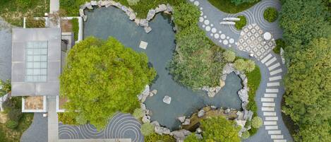 An aerial view of a landscaped area with a central pond, stone pathways, and surrounding greenery.