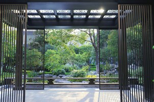 Un jardín japonés tradicional con un portón de madera, un sendero de piedra y abundante vegetación.