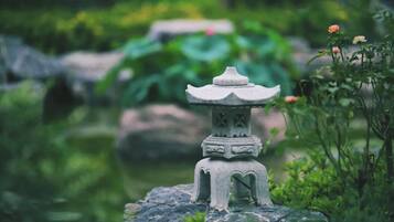 Un farol de piedra en un jardín con follaje y un estanque al fondo.