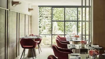 Un espace repas avec des tables et des chaises, de grandes fenêtres et une vue sur la verdure.