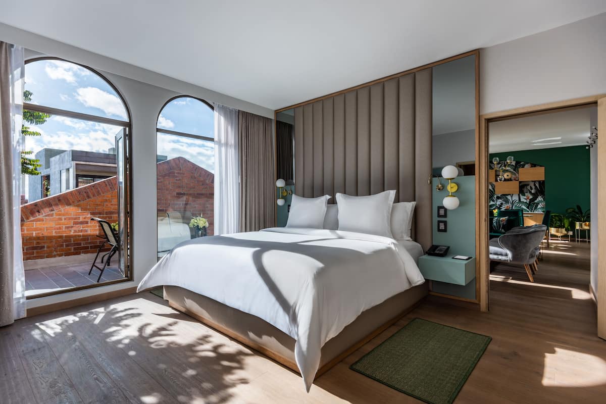 A modern hotel room with a large bed, a sliding glass door to a balcony, and a view of a brick building.
