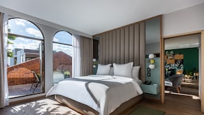 A modern hotel room with a large bed, a sliding glass door to a balcony, and a view of a brick building.