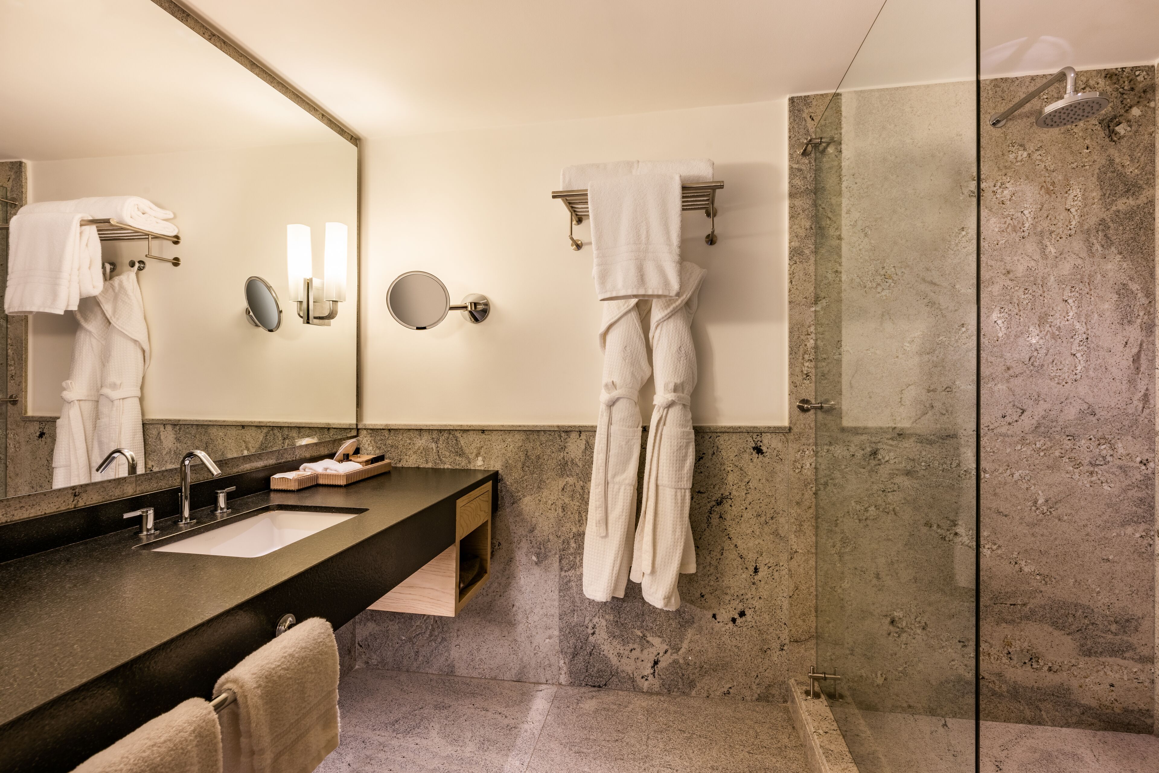 Un baño moderno con un espejo grande, lavamanos dobles y ducha con cerramiento de vidrio.