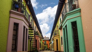 A narrow street flanked by colorful buildings with balconies, a clear sky, and a cobblestone path.