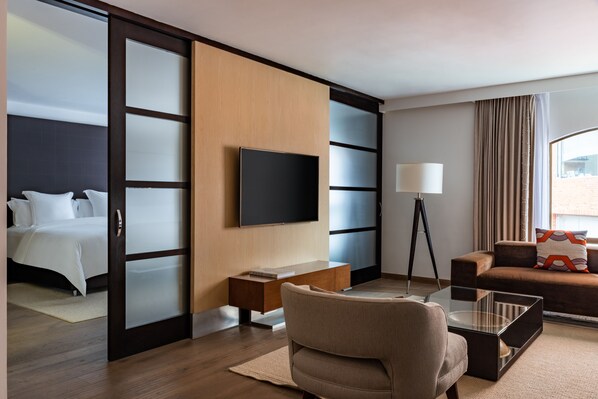 A hotel room with a bed, a sofa, a TV, a desk, and a lamp.
