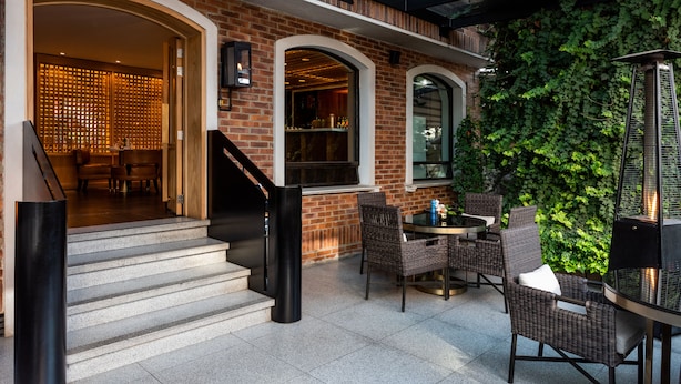 A brick building with a glass-enclosed patio area featuring wicker furniture and a fireplace.