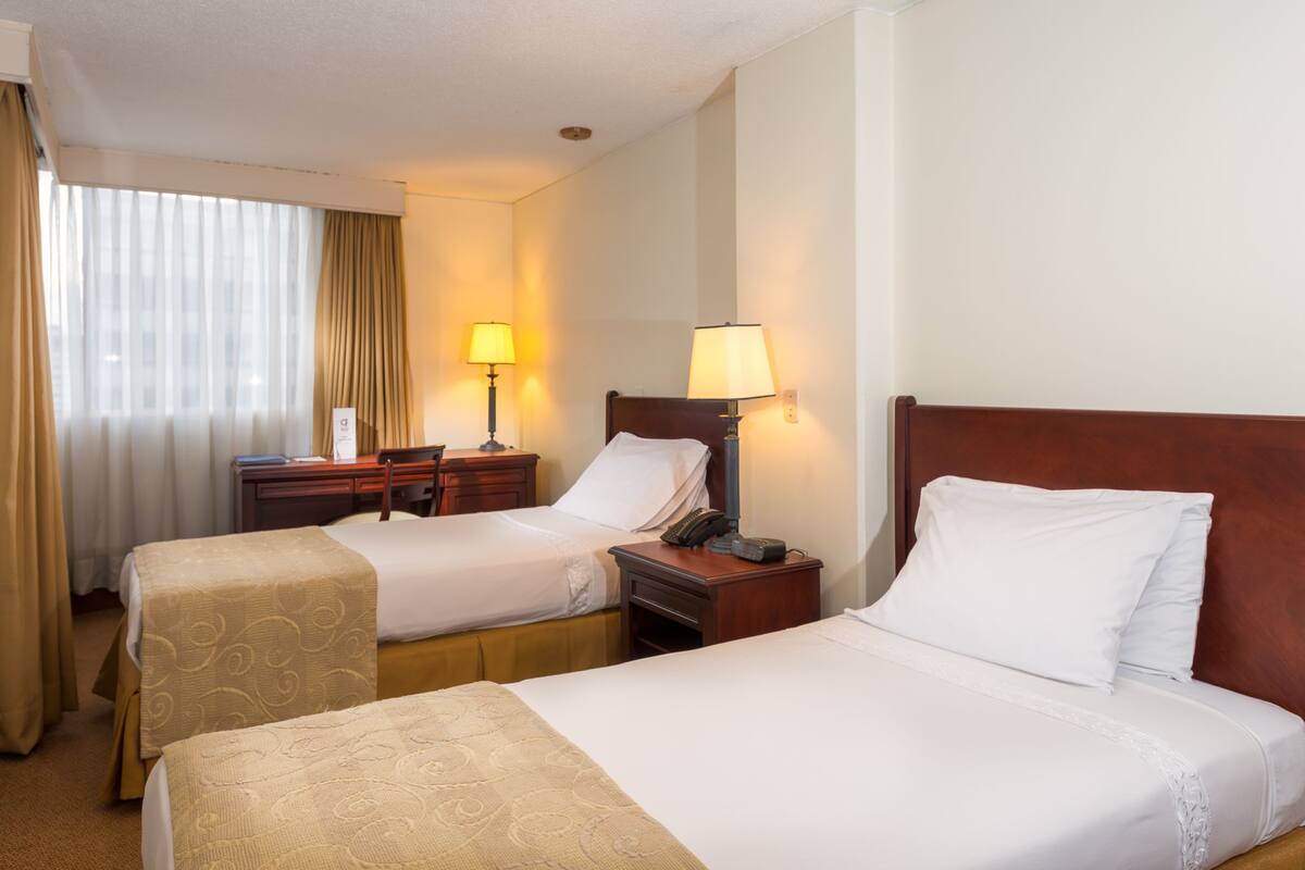 Habitación de hotel con dos camas, un escritorio, una silla y una ventana con cortinas.