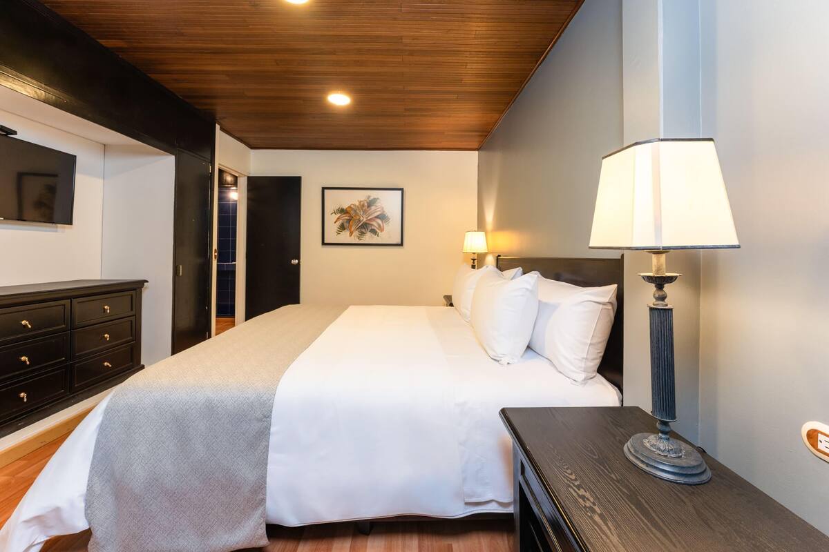 Un dormitorio con cama, lámparas de noche, cómoda y televisor en la pared.