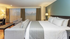 Una habitación de hotel con una cama, dos sillones, un escritorio y una lámpara.