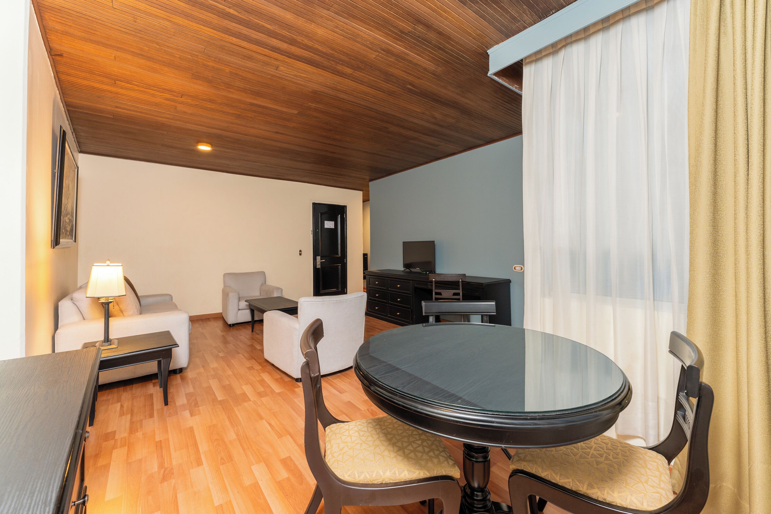 Un salon moderne avec une table ronde, deux chaises, un canapé, un téléviseur et un plafond en bois.