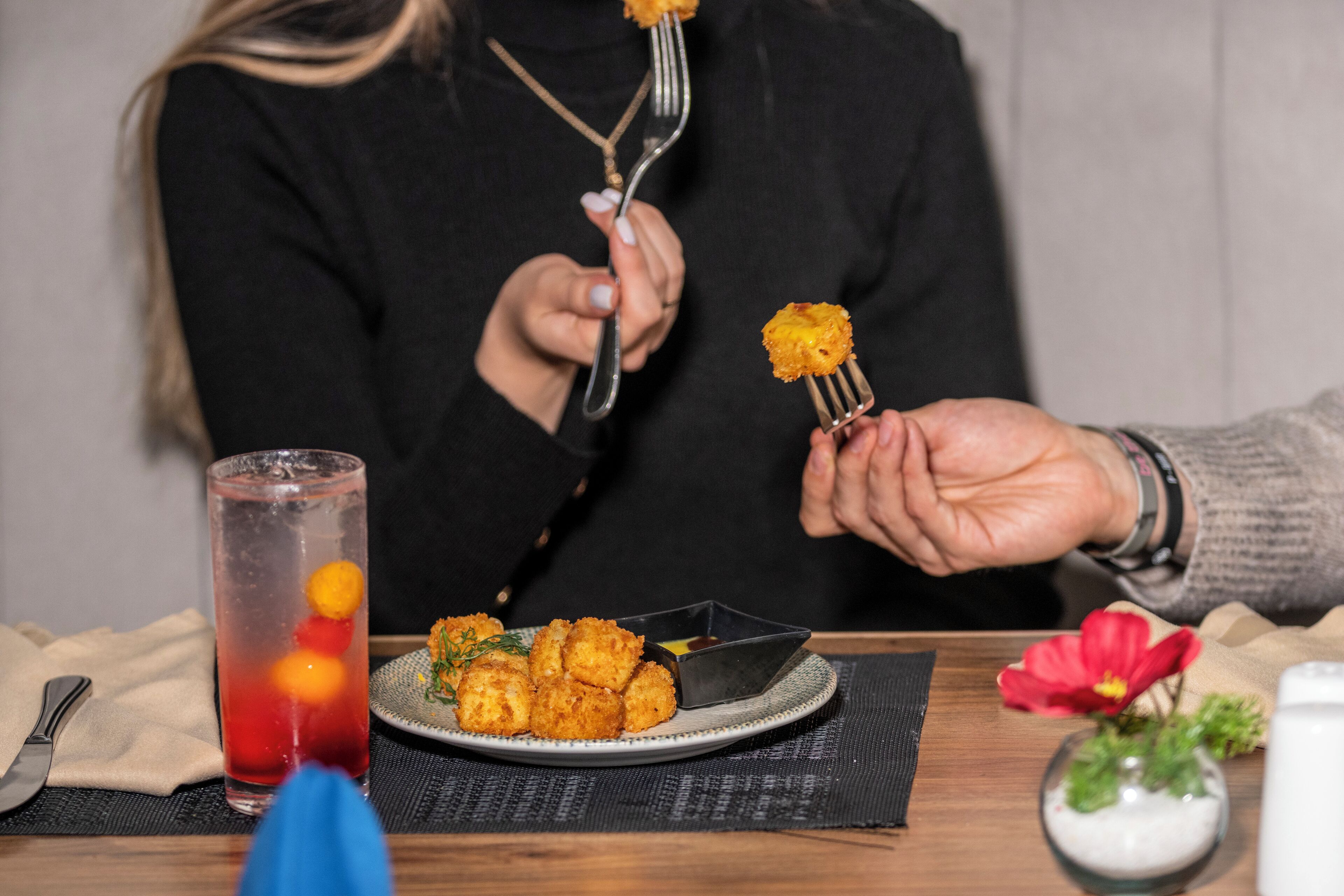 Een eettafel met een bord eten, een glas rode drank en een kleine vaas met een bloem.