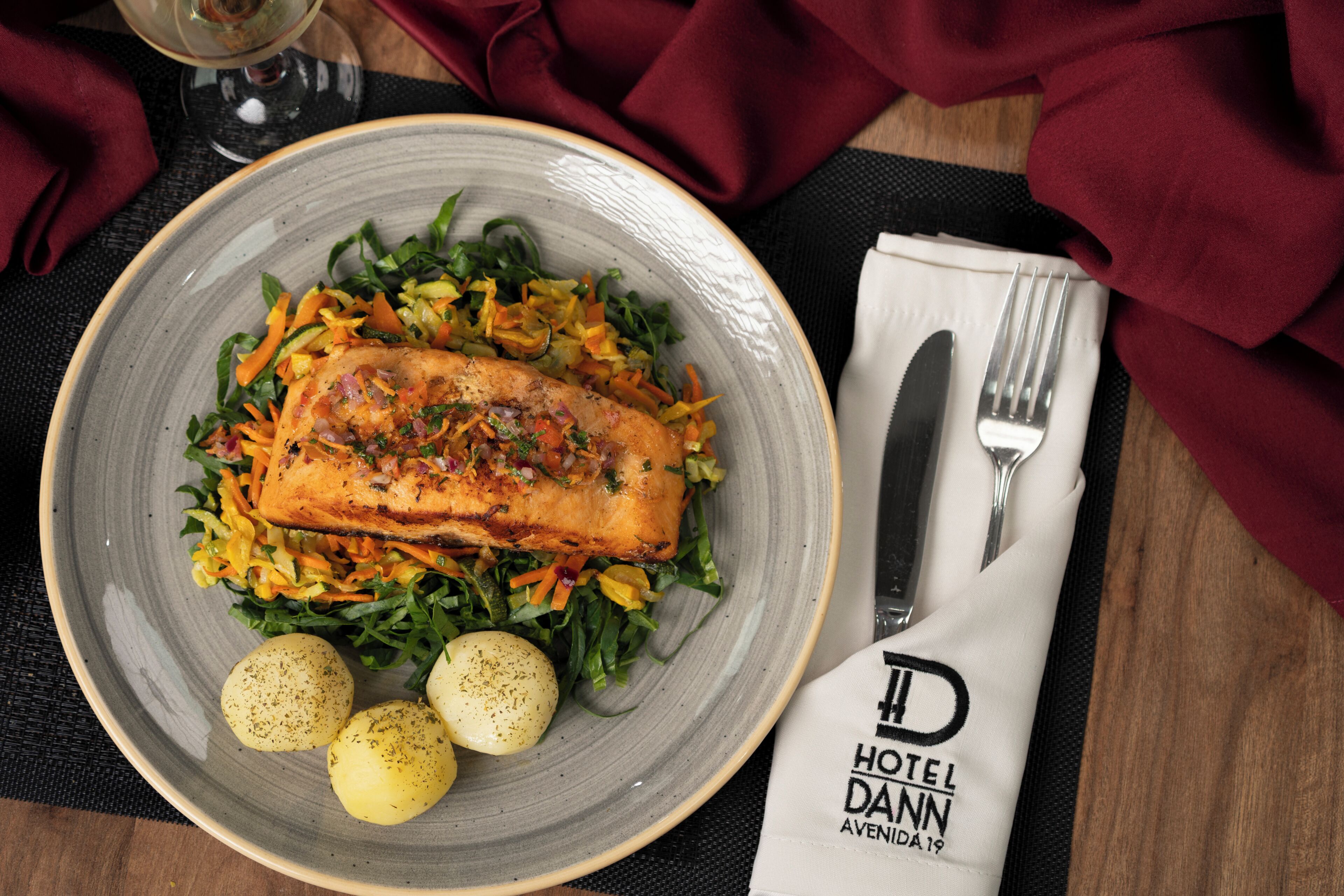 A plate of food with a fish fillet and vegetables, a fork, and a napkin with a hotel logo.