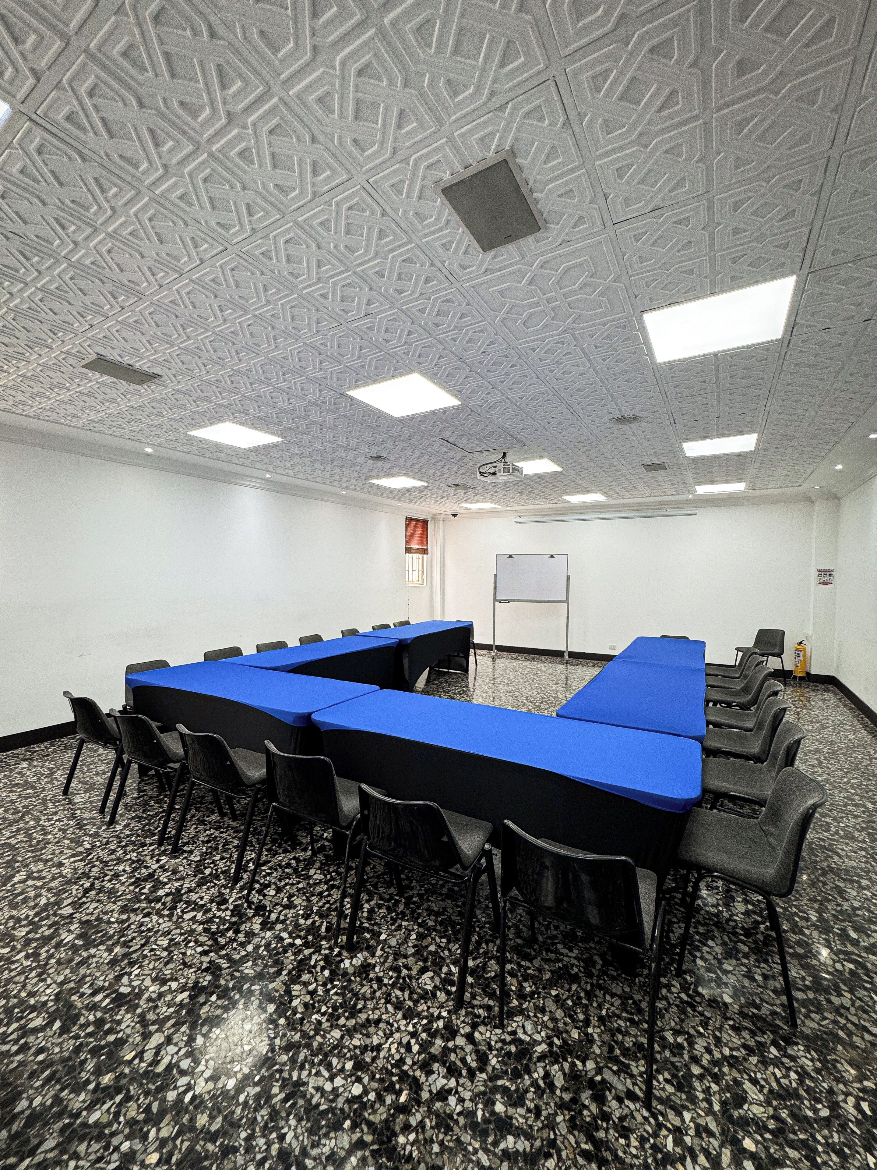 Un salón de conferencias con techo de diseño geométrico, una pizarra y un proyector.