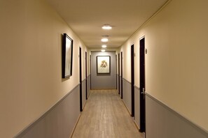 Un couloir d’hôtel avec des œuvres d’art encadrées accrochées aux murs, des portes des deux côtés et une moquette de couleur claire.