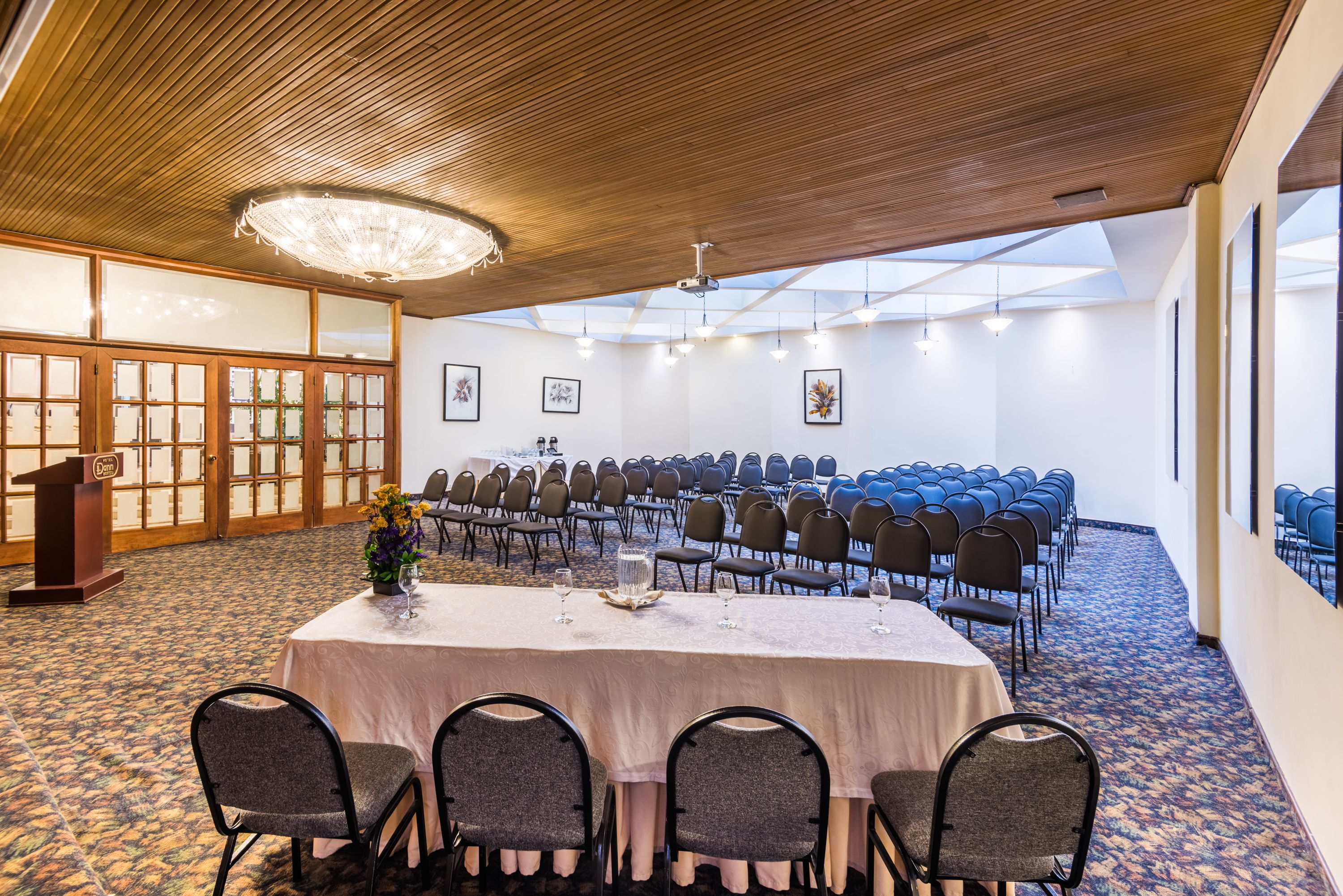 Un salón de conferencias con una larga mesa, sillas, un atril y cuadros en las paredes.