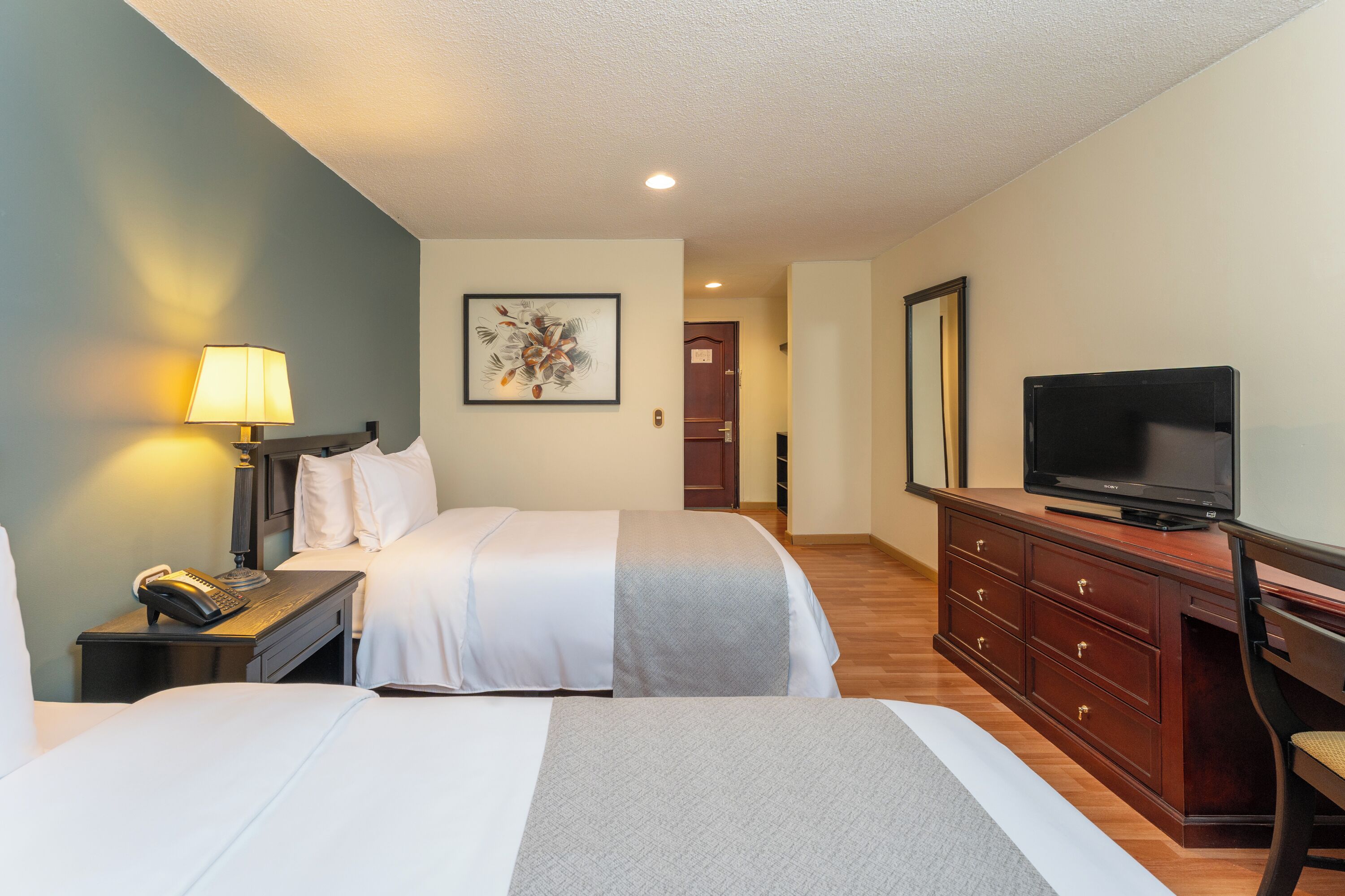 A hotel room with two beds, a desk with a lamp, a television, and a dresser.