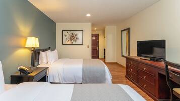 A hotel room with two beds, a desk with a lamp, a television, and a dresser.