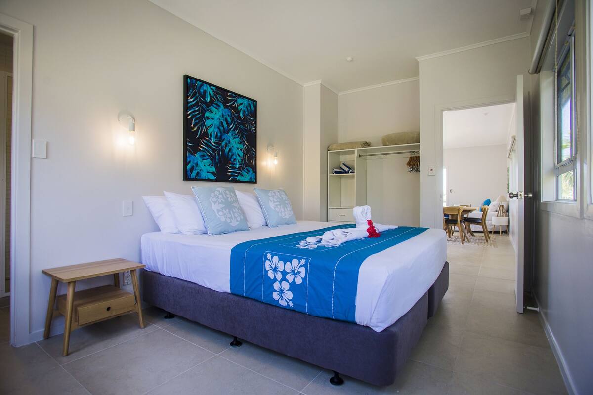 A modern bedroom with a bed, bedside table, and a large painting on the wall.
