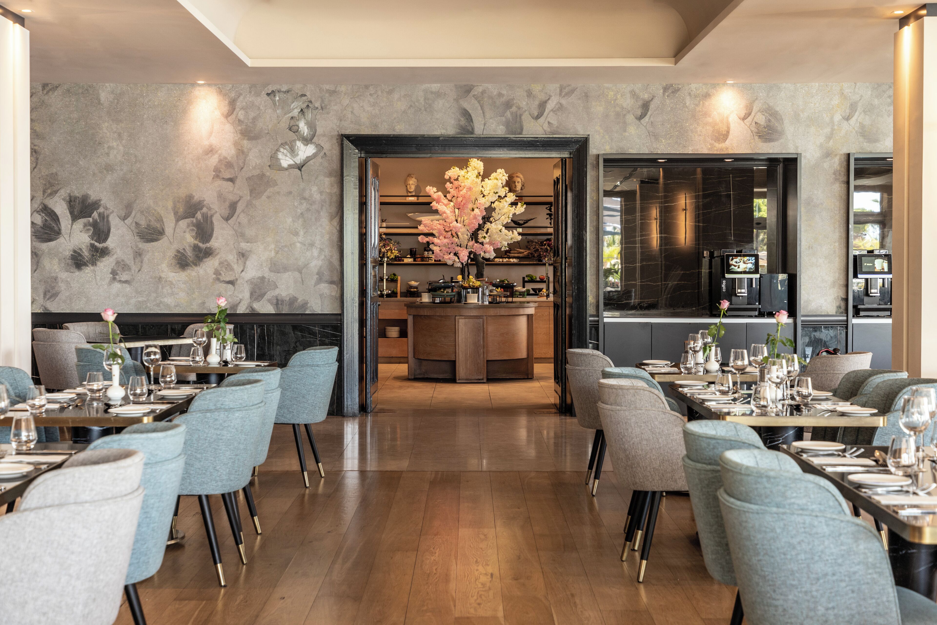 Un restaurante moderno con una zona de bar central, suelo de madera y sillas tapizadas en gris.