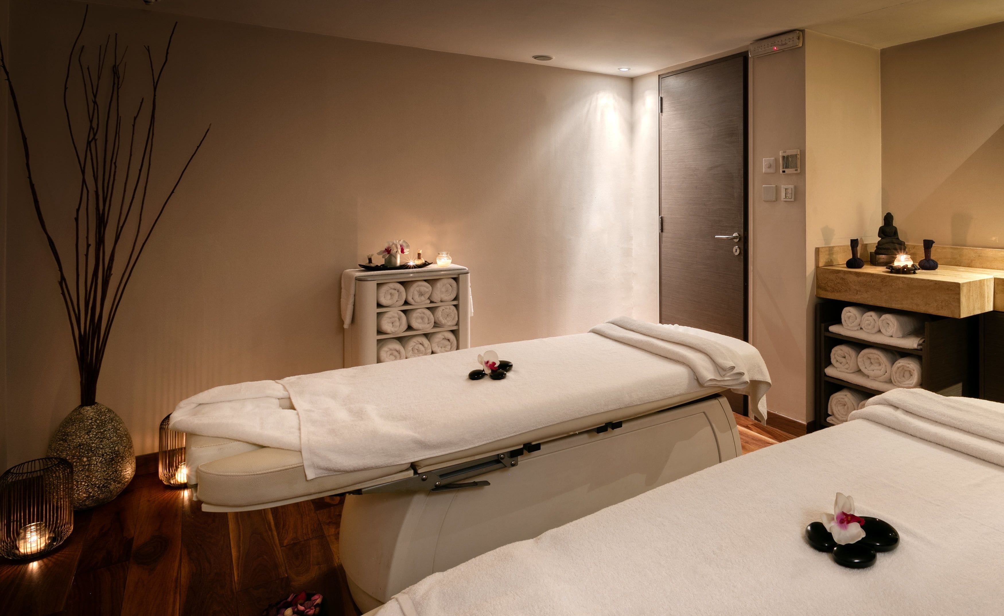 Un cuarto de spa con dos camillas, un estante con toallas, una estatua y un pequeño altar con velas.