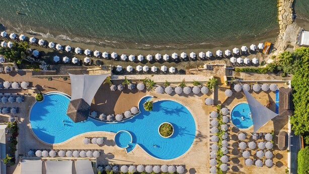 Oversigtsbillede af et resort med en stor swimmingpool, strandparasoller og liggestole.