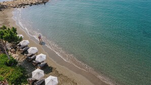 En strand med klart vand, en klippefyldt bølgebryder og flere parasoller samt liggestole.