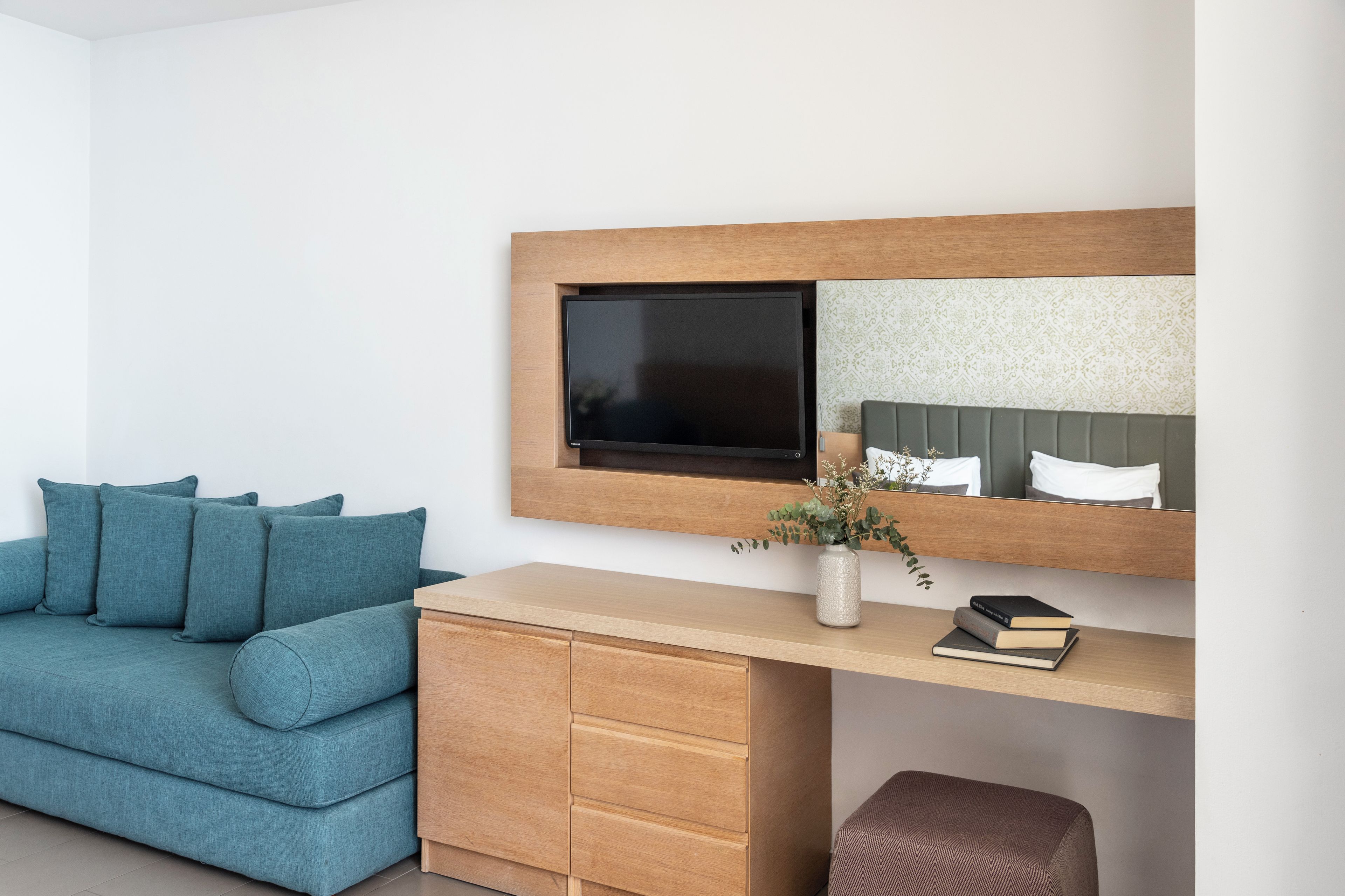 Una habitación moderna con sofá, un escritorio de madera, un espejo y una planta pequeña.