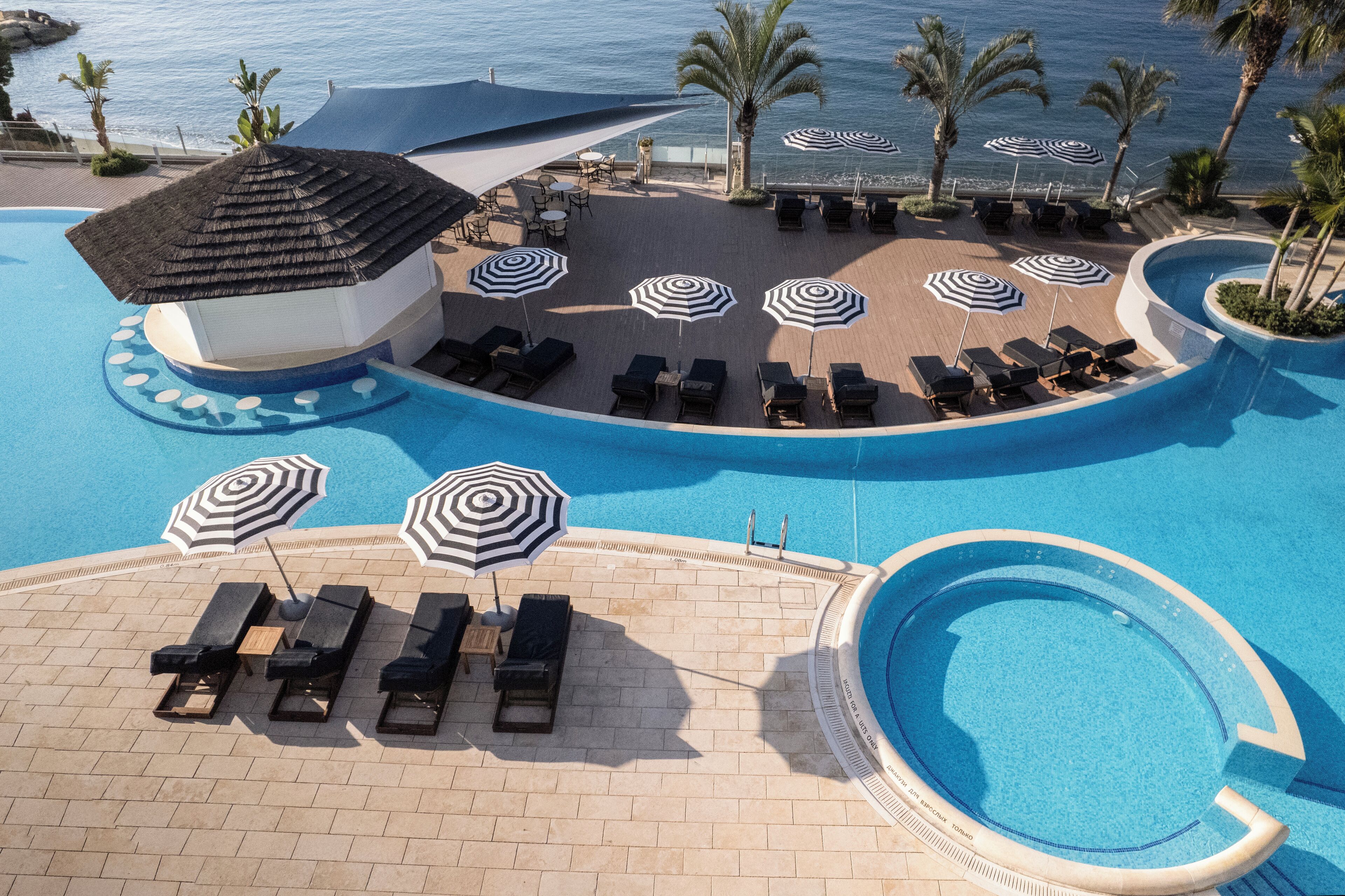 Area piscina di un resort con lettini, ombrelloni e vista sull'oceano.