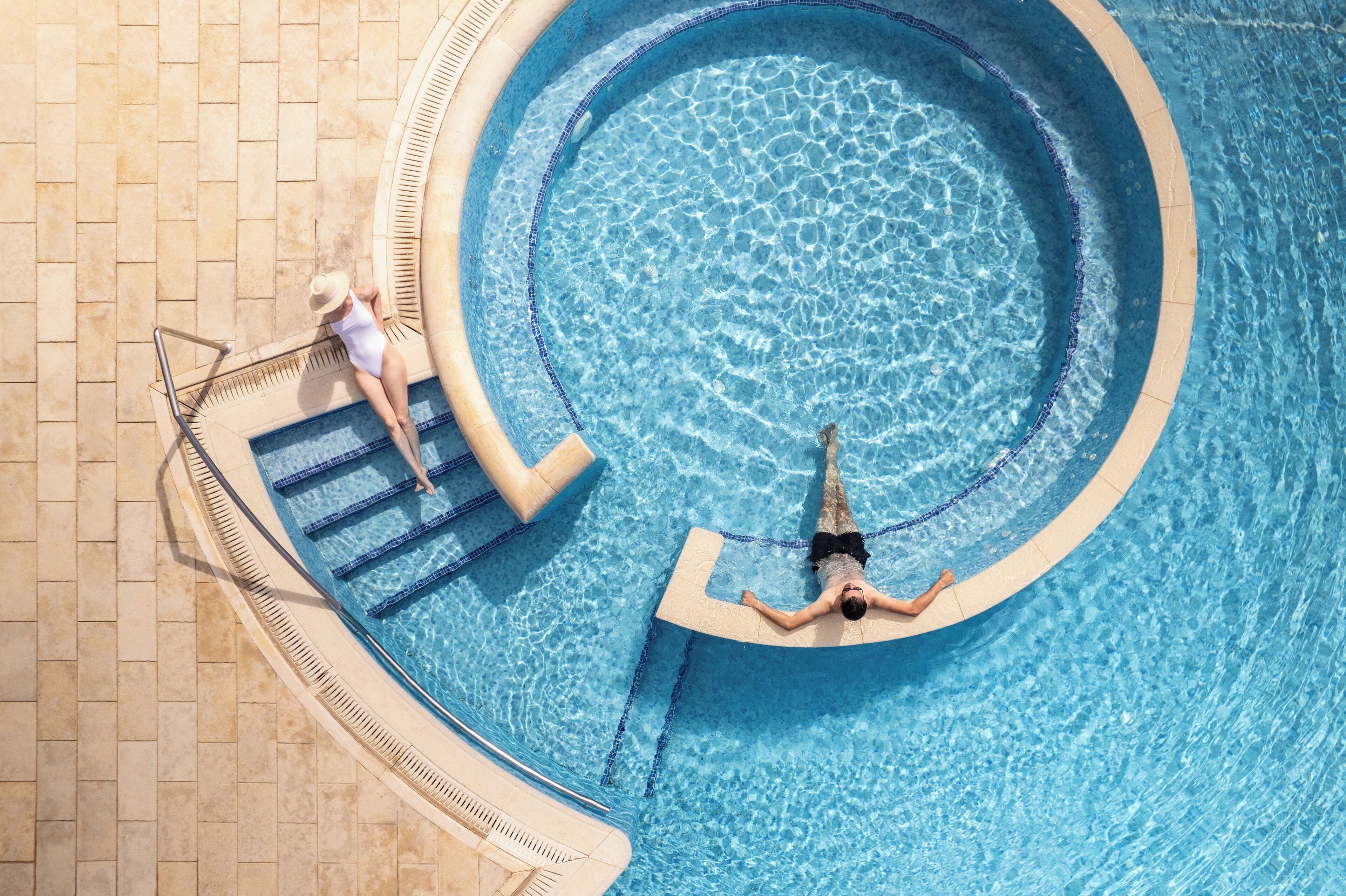 Piscina circular com um deck ladrilhado e uma pessoa deitada na borda.