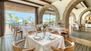 A restaurant with tables set for dining, large windows, and a view of the ocean.