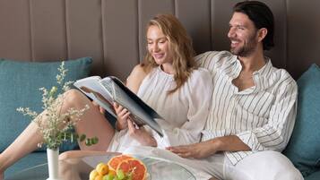 A couple sitting on a sofa with a glass table in front of them, a book, and a plate of fruit.