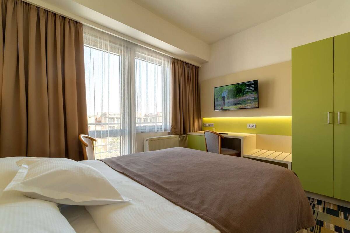 Una habitación de hotel con cama, escritorio, silla, televisor y armario.