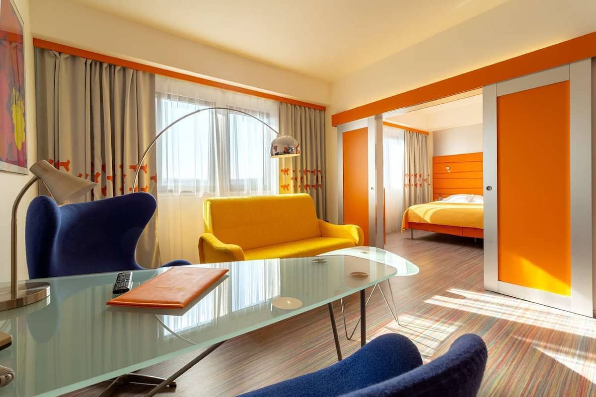Una habitación de hotel con una mesa de vidrio, un sofá, una cama y un escritorio con una lámpara.