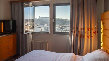 A hotel room with a bed, a TV, and a window with a view of a city and a hill.
