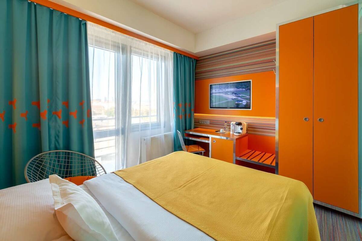 Habitación de hotel con cama, escritorio, silla, televisor y armario.