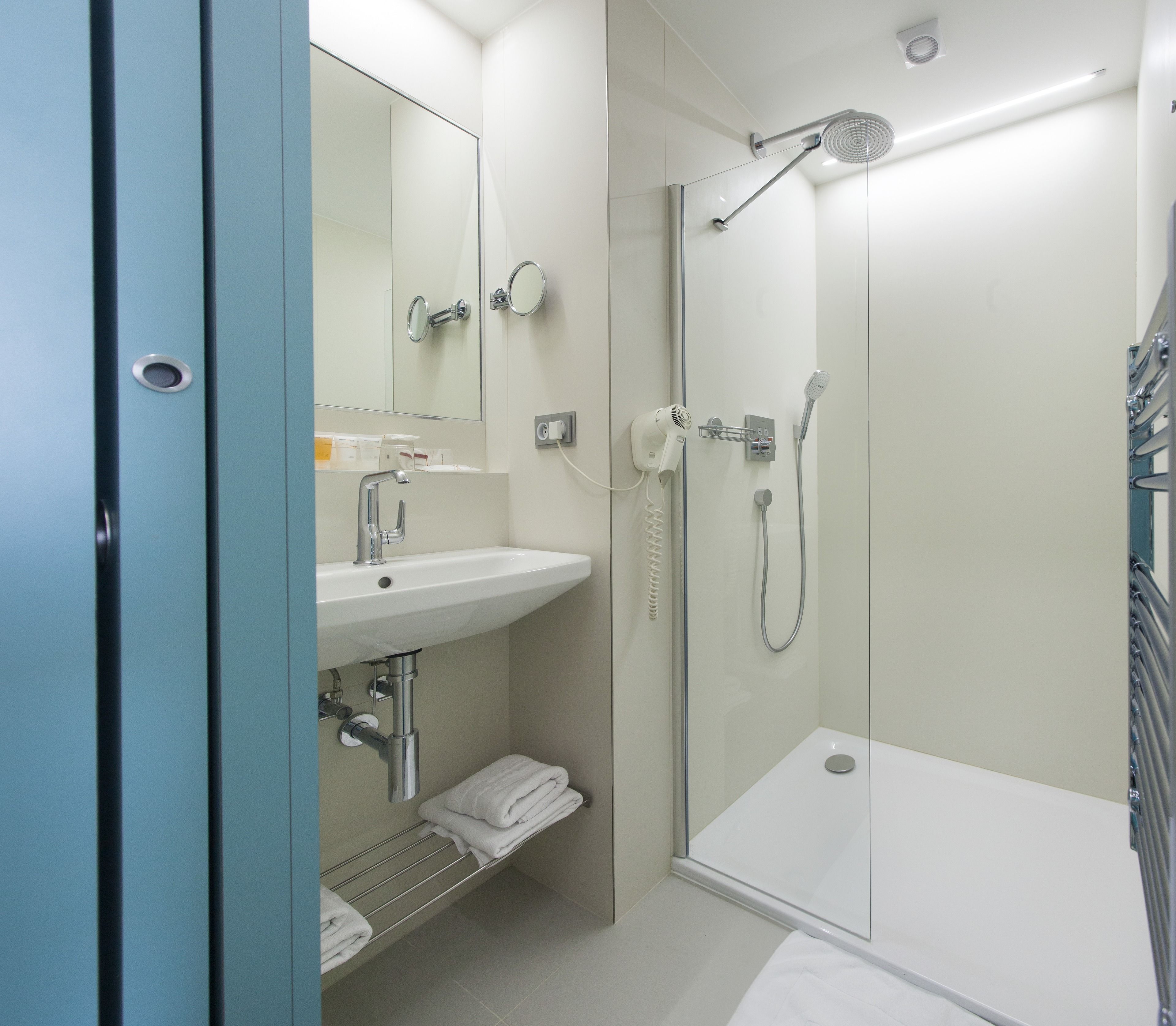 Un baño moderno con ducha envuelta en vidrio, un lavabo con espejo y un perchero para toallas.