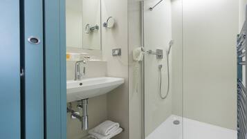 A modern bathroom with a glass-enclosed shower, a sink with a mirror, and a towel rack.
