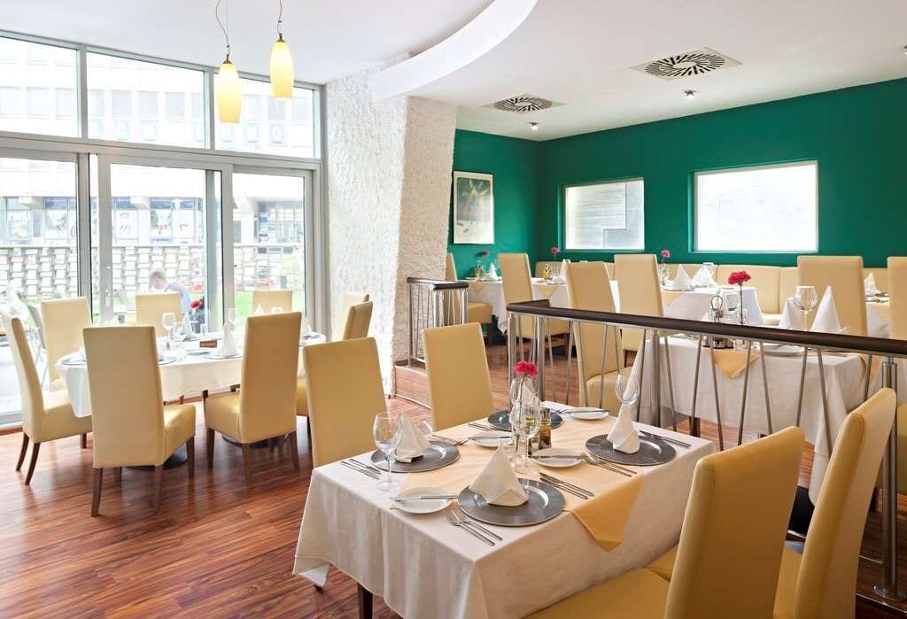 Un restaurante con mesas redondas, sillas amarillas y una pared verde.