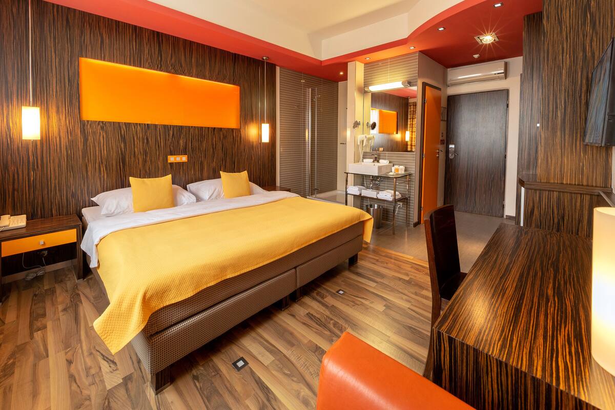 Una habitación de hotel moderna con una cama grande, un escritorio y un baño con espejo y lavabo.